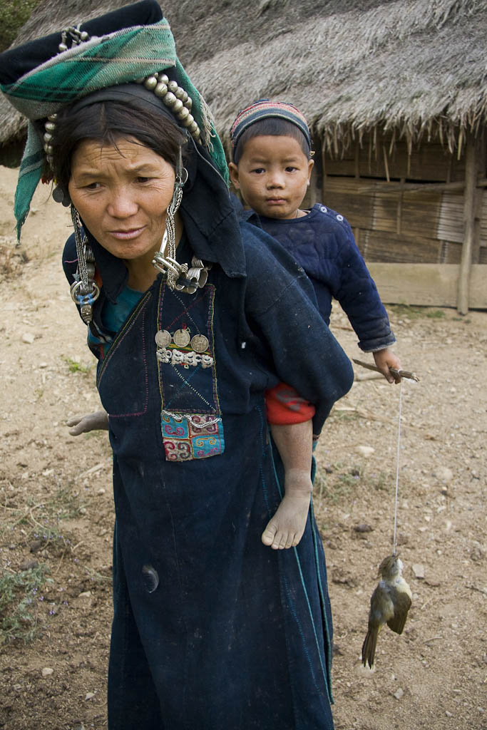 A woman holds a kid in her back. The child is playing with a dead bird. Mountains Between Phongsali and Chinese border. Laos.